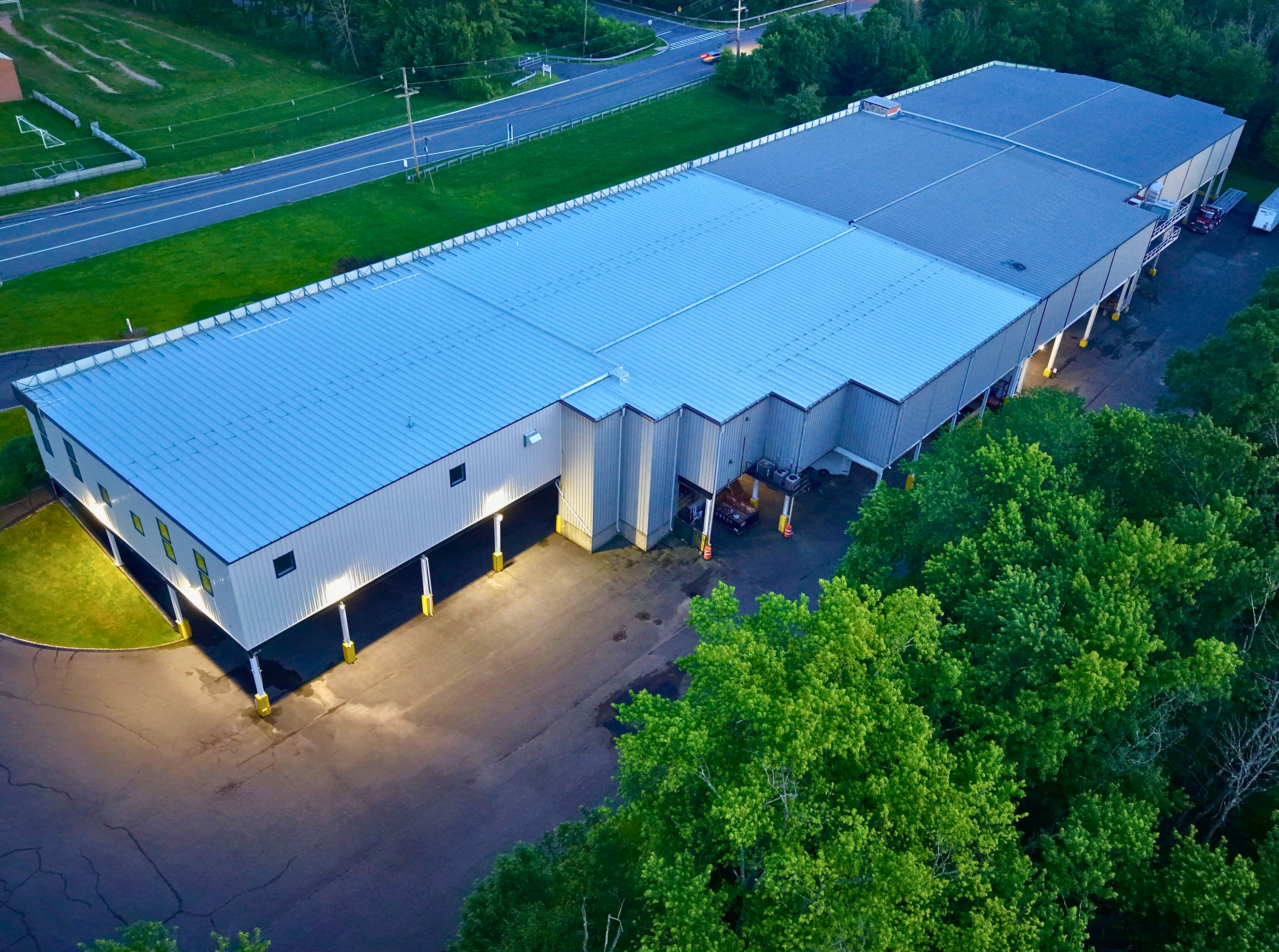 Aerial view of a large commercial building with a metal roof, surrounded by trees and a roadway.